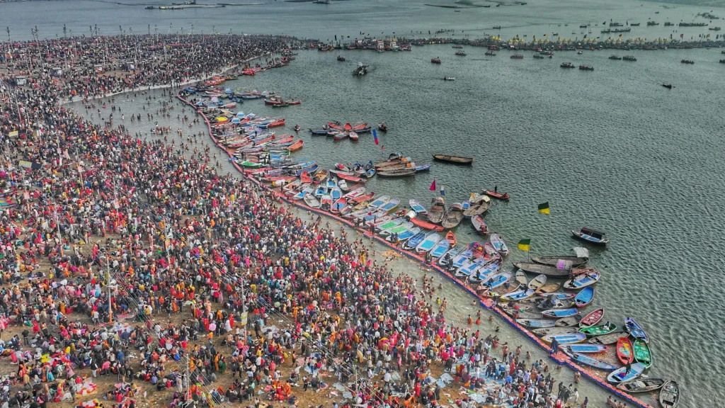 A large crowd of devotees bathing in a sacred river during the Kumbh Mela. crowds of people and temporary infrastructure set up for the event.