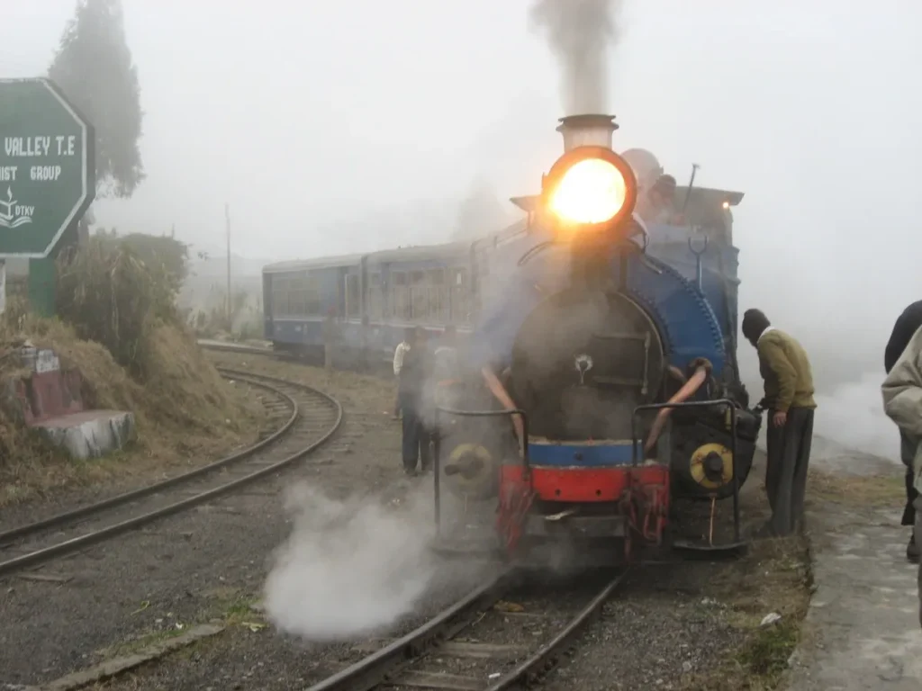 Darjeeling Himalayan Railway toy train passing through Batasia Loop with Kanchenjunga in the background.